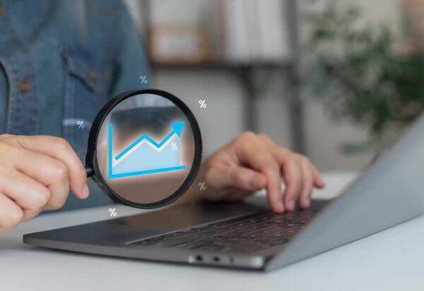 A woman analyzing a financial growth chart on a laptop with a magnifying glass, concept of business performance, data analytics, and percentage statistics.