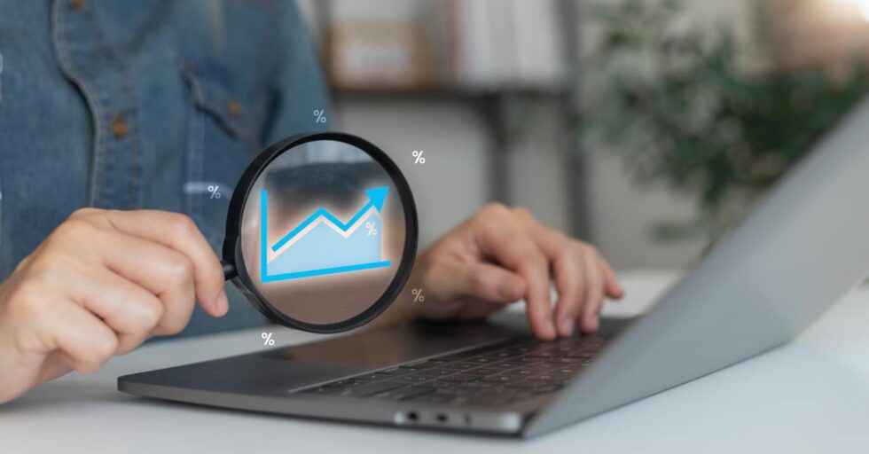 A woman analyzing a financial growth chart on a laptop with a magnifying glass, concept of business performance, data analytics, and percentage statistics.